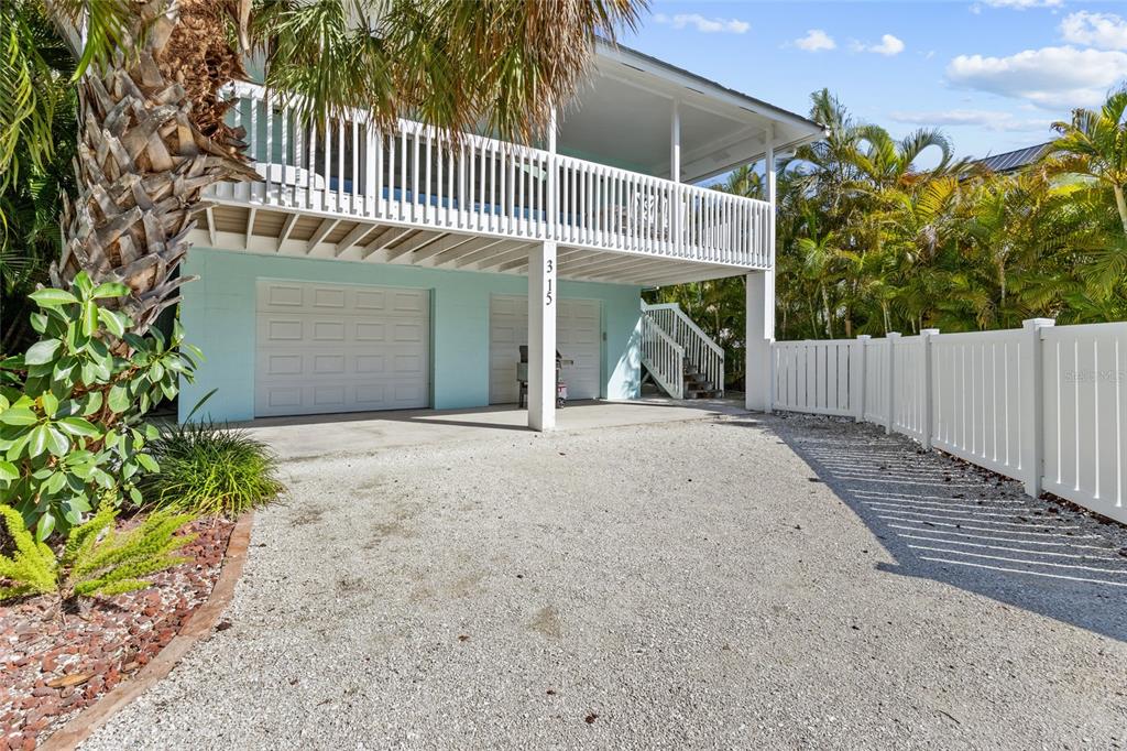 A light blue elevated house with a gravel driveway and a white vinyl fence — 315 SPRING AVENUE, ANNA MARIA, FL