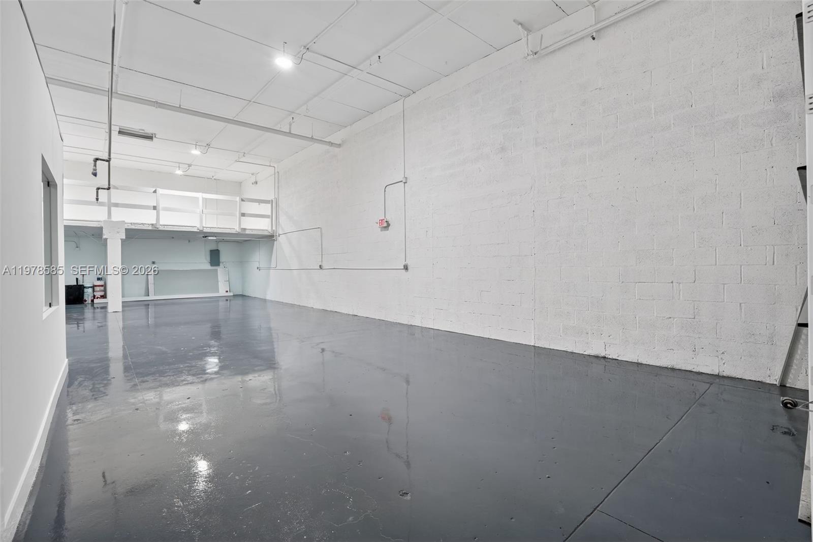 An empty industrial warehouse space features a concrete floor, white brick walls, and a mezzanine — 16300 SW 137th Ave # 119, Miami FL 33177, MIAMI, FL
