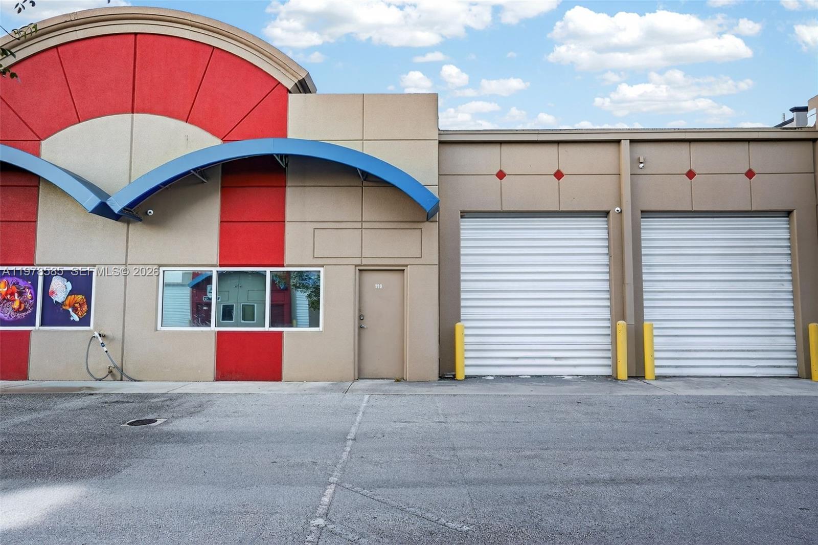 The exterior of a commercial building features a tan facade, red accents, and two roll-up doors — 16300 SW 137th Ave # 119, Miami FL 33177, MIAMI, FL