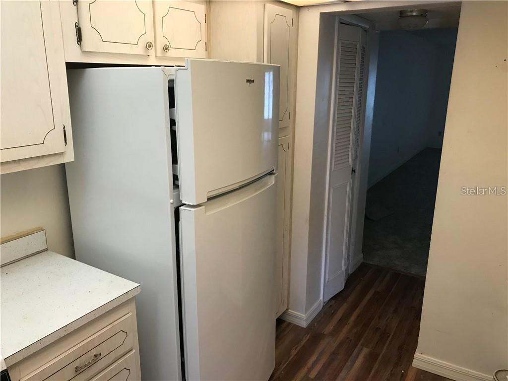 A white refrigerator stands in a kitchen with wood-look flooring and white cabinets — 1100 MARTINIQUE DRIVE UNIT 117, WINTER HAVEN, FL
