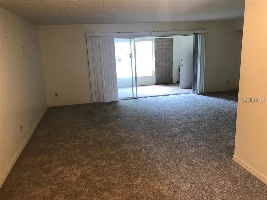 An empty living room features beige carpeting and a sliding glass door to a patio — 1100 MARTINIQUE DRIVE UNIT 117, WINTER HAVEN, FL