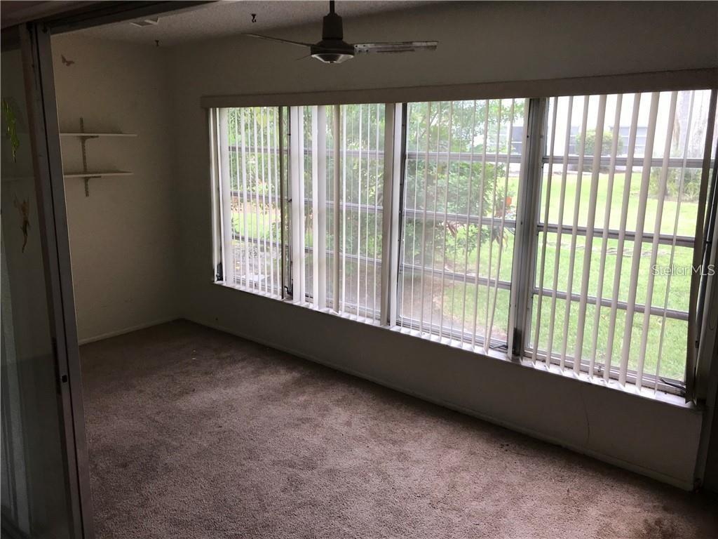 A carpeted room features a large window wall with vertical blinds and a ceiling fan — 1100 MARTINIQUE DRIVE UNIT 117, WINTER HAVEN, FL