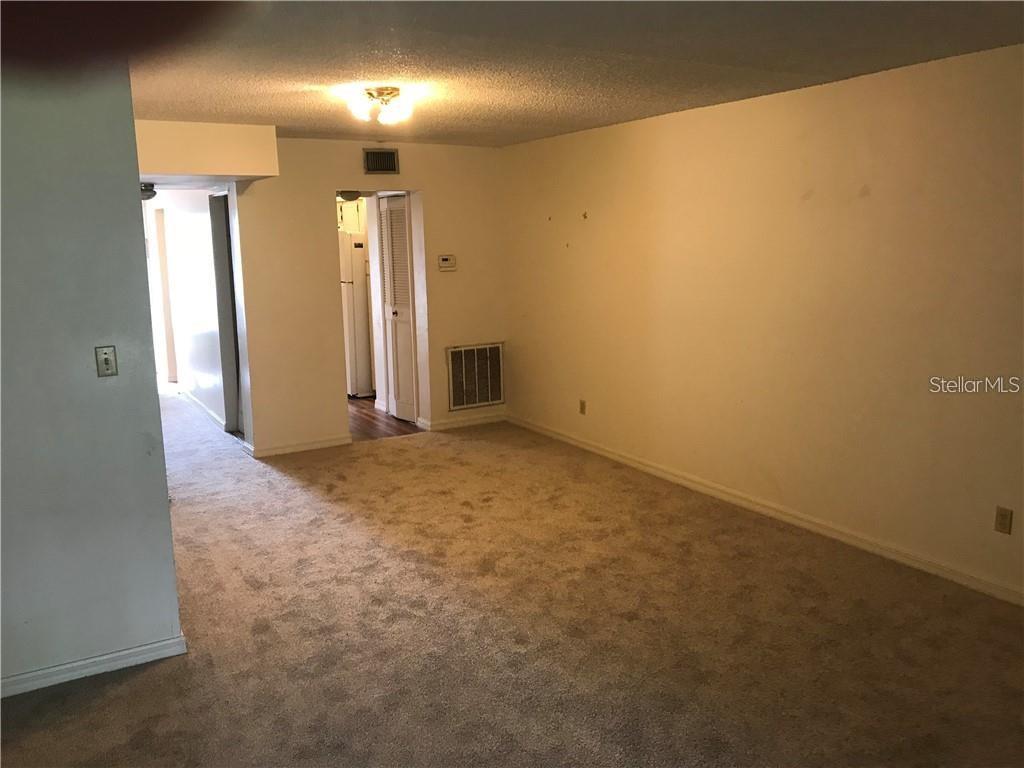 An empty room with beige carpet, white walls, and a doorway leading to a kitchen — 1100 MARTINIQUE DRIVE UNIT 117, WINTER HAVEN, FL
