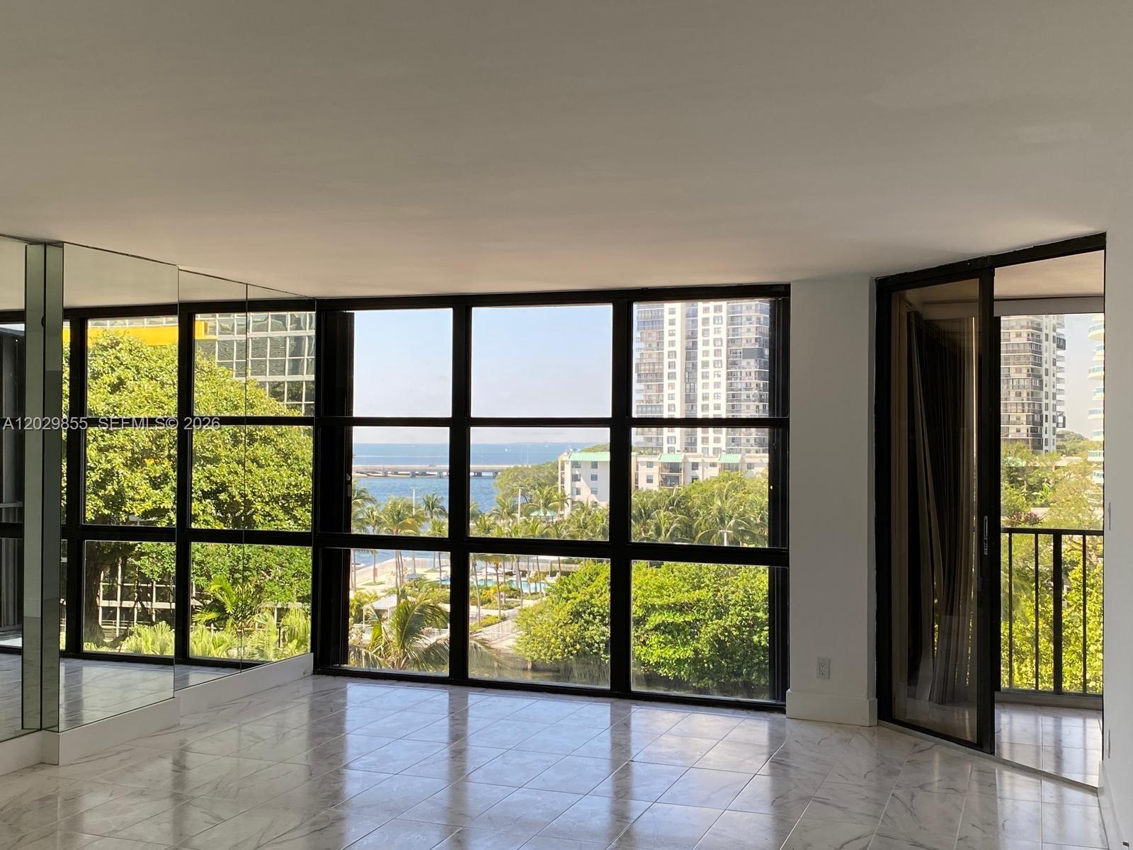 An empty room with marble floors, mirrored walls, and large windows overlooking a coastal view — 1925 Brickell Ave # D610, Miami FL 33129, MIAMI, FL