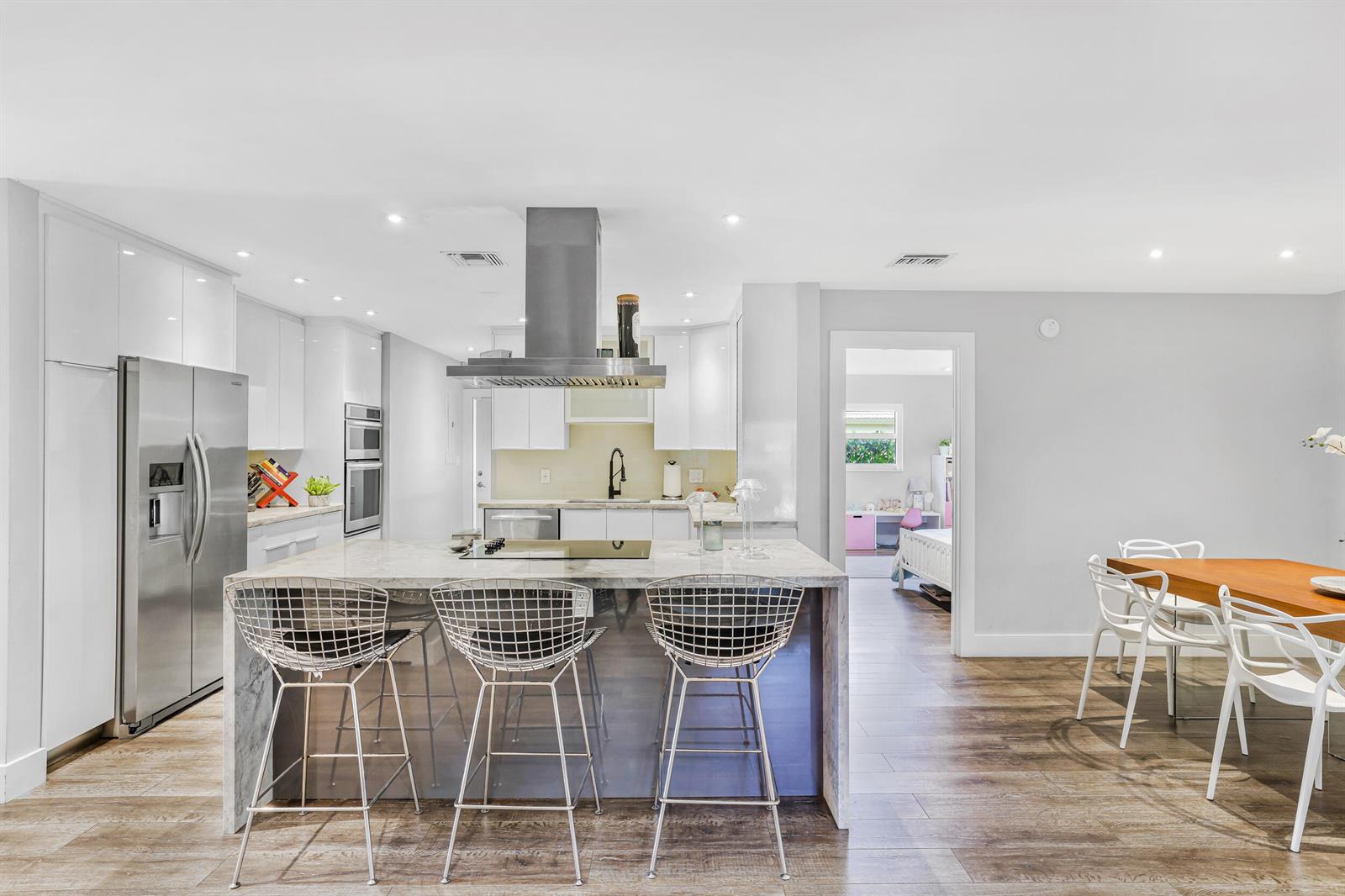 A modern kitchen features a marble-topped island with three wire stools and stainless appliances — 908 Cypress Grove Drive, Pompano Beach FL 33069, POMPANO BEACH, FL