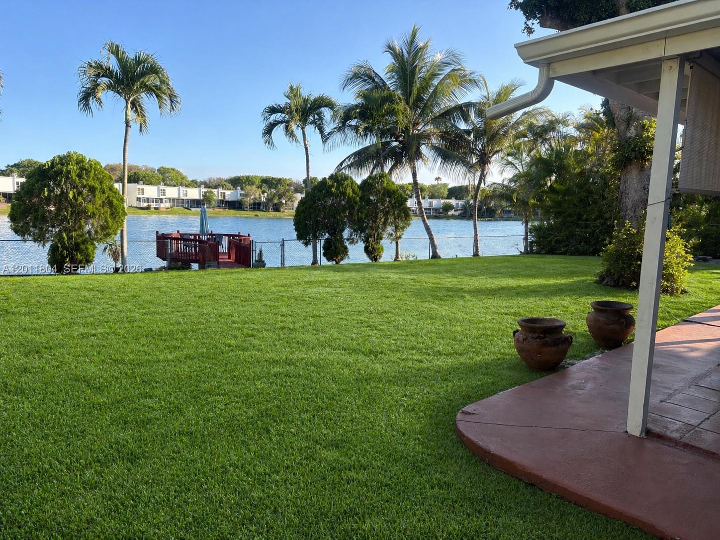 A grassy backyard features palm trees, a small wooden deck, and a view of water — 14020 SW 83rd St, Miami FL 33183, MIAMI, FL