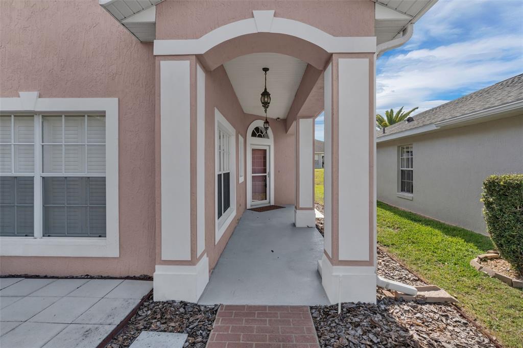 A covered entryway with a pink stucco exterior, white trim, and a brick walkway — 213 HIGH VISTA DR, DAVENPORT, FL