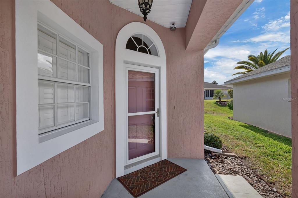 A pink stucco exterior wall features a white arched front door and a nearby window — 213 HIGH VISTA DR, DAVENPORT, FL