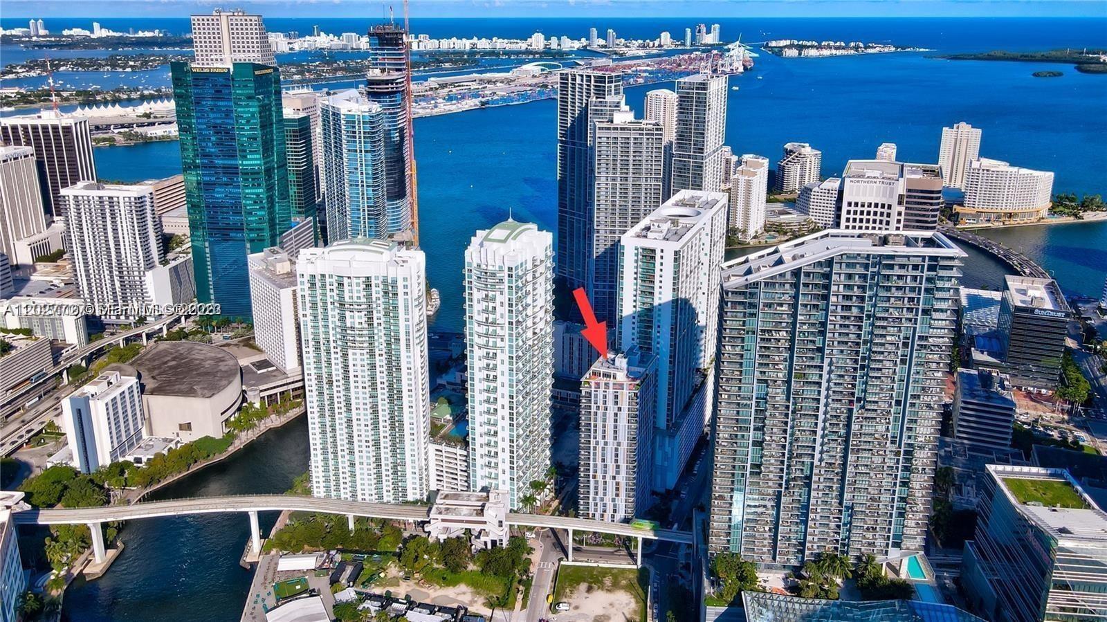 An aerial view of a dense urban waterfront with numerous high-rise buildings and a red arrow — 31 SE 6th St # 505, Miami FL 33131, MIAMI, FL