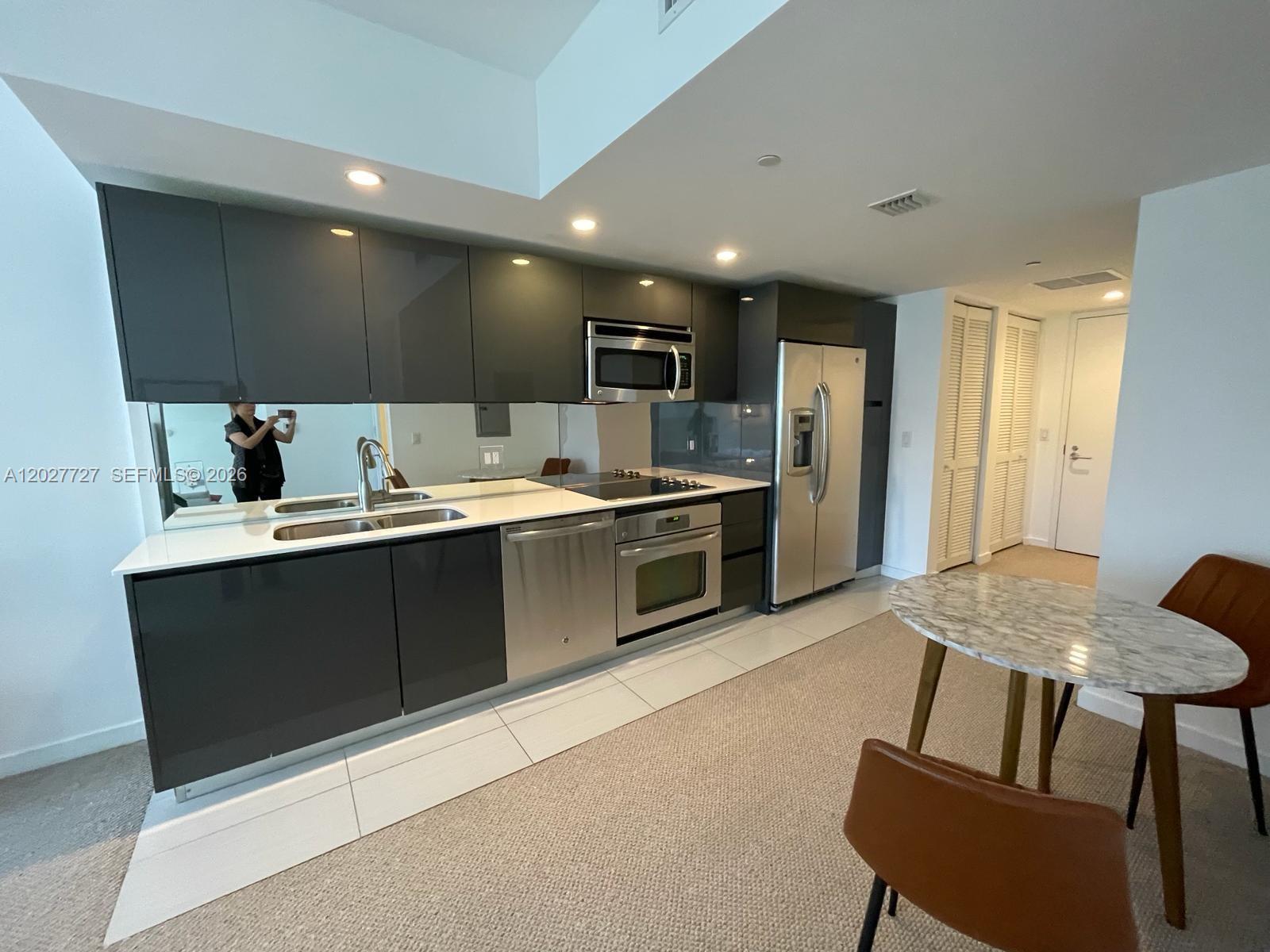 A modern kitchen features dark gray cabinetry, stainless steel appliances, and a marble-topped dining table — 31 SE 6th St # 505, Miami FL 33131, MIAMI, FL