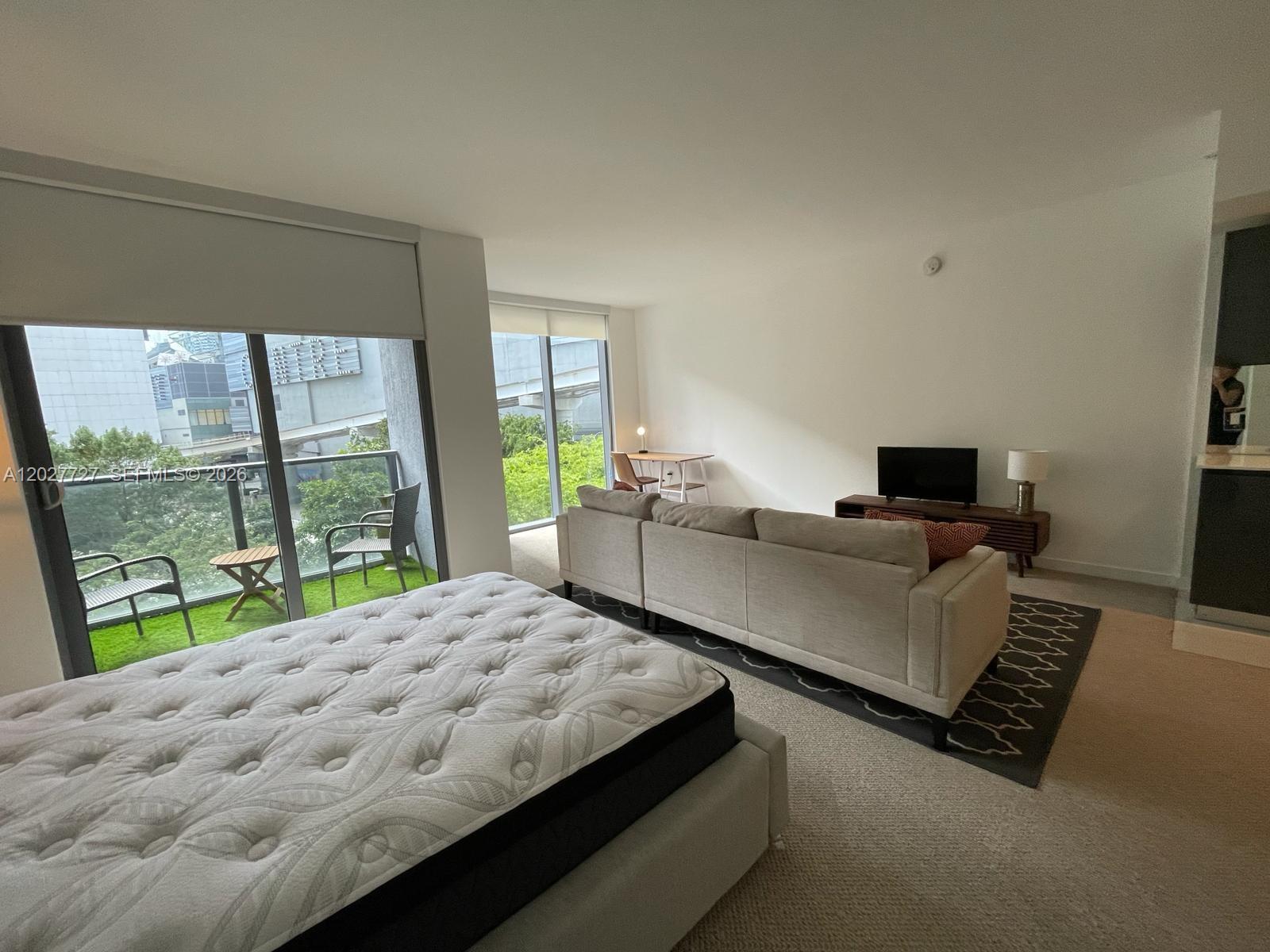A studio apartment features a bed, a sofa, a television, and a balcony with outdoor seating — 31 SE 6th St # 505, Miami FL 33131, MIAMI, FL