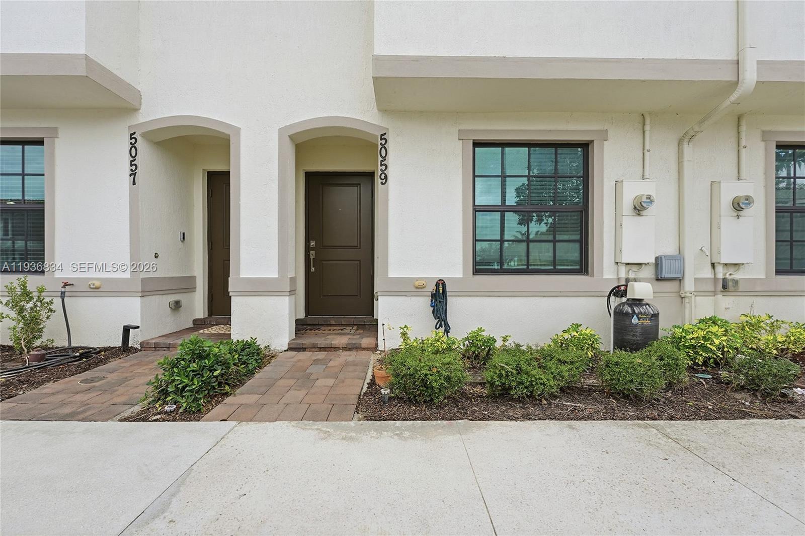 The exterior view shows two adjacent townhome entrances with brown doors and paved walkways — 5059 Genove Pl, Riviera Beach FL 33410, RIVIERA BEACH, FL