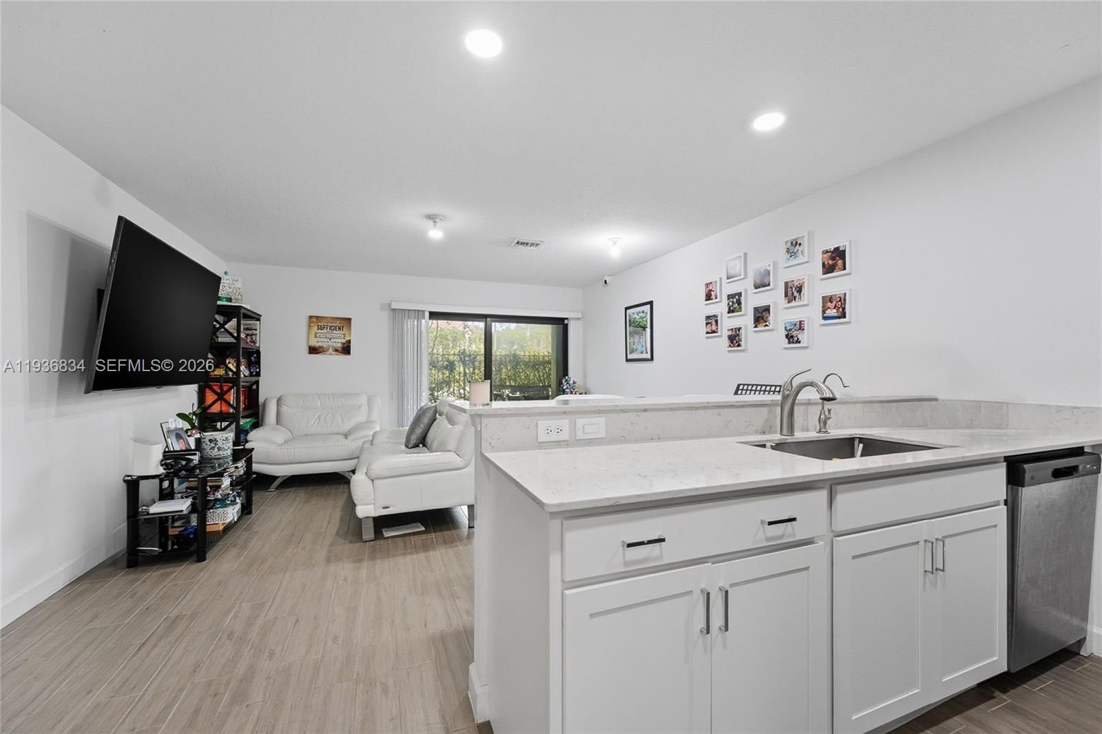 A kitchen with white cabinets and quartz countertops overlooks a living area with white furniture — 5059 Genove Pl, Riviera Beach FL 33410, RIVIERA BEACH, FL