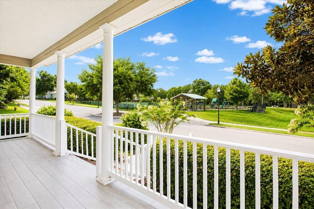 A covered porch with white railings overlooks a neighborhood street, green lawn, and playground — 16704 NW 166TH ROAD, ALACHUA, FL