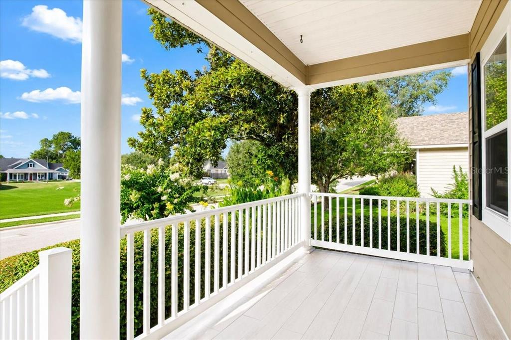 A covered front porch with white railings, columns, and light-colored tile flooring — 16704 NW 166TH ROAD, ALACHUA, FL