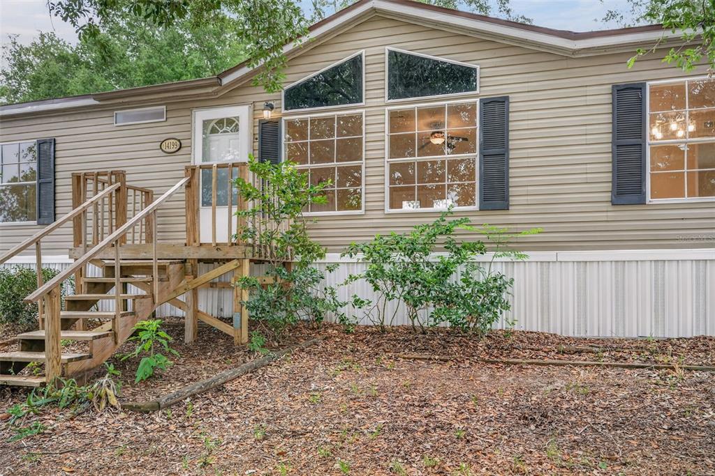 A tan manufactured home features a wooden staircase leading to the front entrance — 14199 SE 59TH COURT, SUMMERFIELD, FL