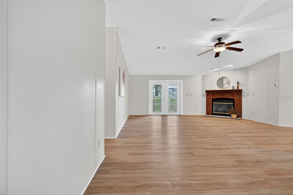 A spacious living room features light wood-look flooring, a vaulted ceiling, and a corner fireplace — 14199 SE 59TH COURT, SUMMERFIELD, FL