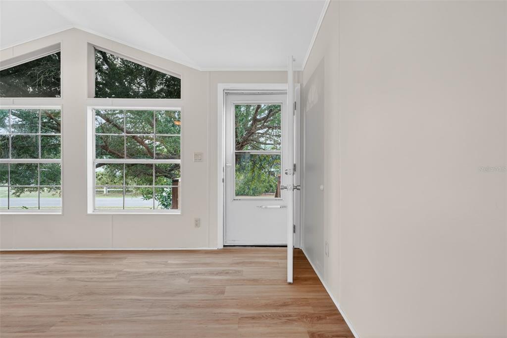 A bright room features light wood-look flooring, large windows, and a glass-paneled exterior door — 14199 SE 59TH COURT, SUMMERFIELD, FL