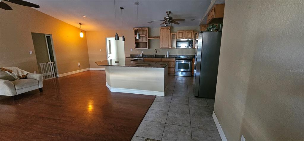An open-concept kitchen features a granite-topped island, wooden cabinetry, and tile flooring — 23077 HAMMOND AVENUE, PORT CHARLOTTE, FL