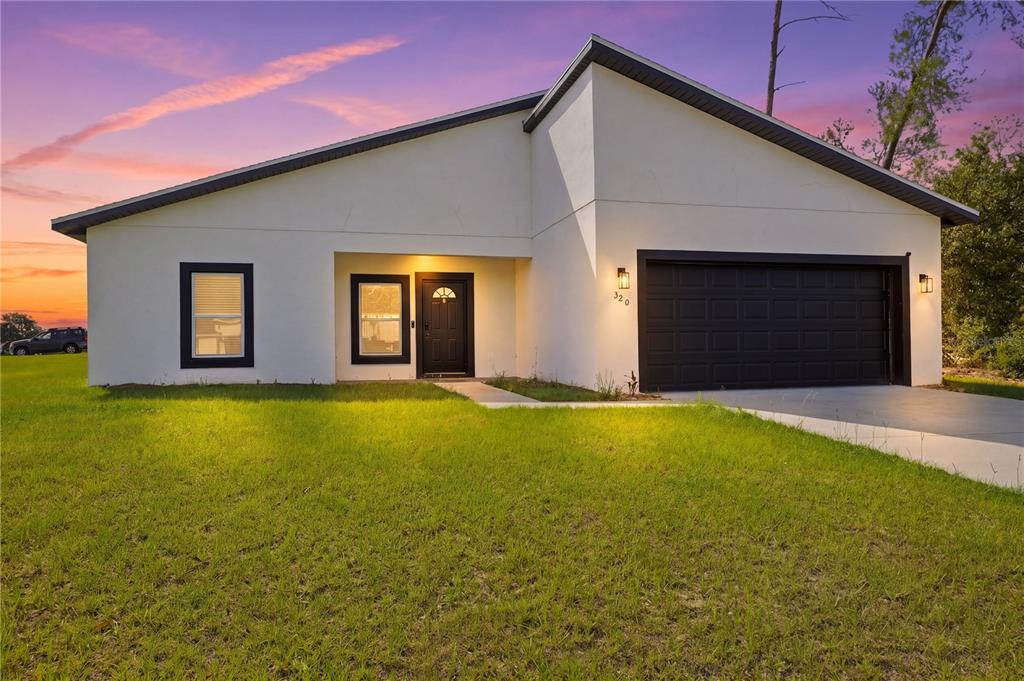 A modern single-story house with white stucco walls, black trim, and a two-car garage — 320 MARION OAKS GOLF ROAD, OCALA, FL