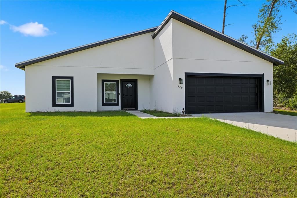 A modern, white single-story house features a black garage door and matching window trim — 320 MARION OAKS GOLF ROAD, OCALA, FL