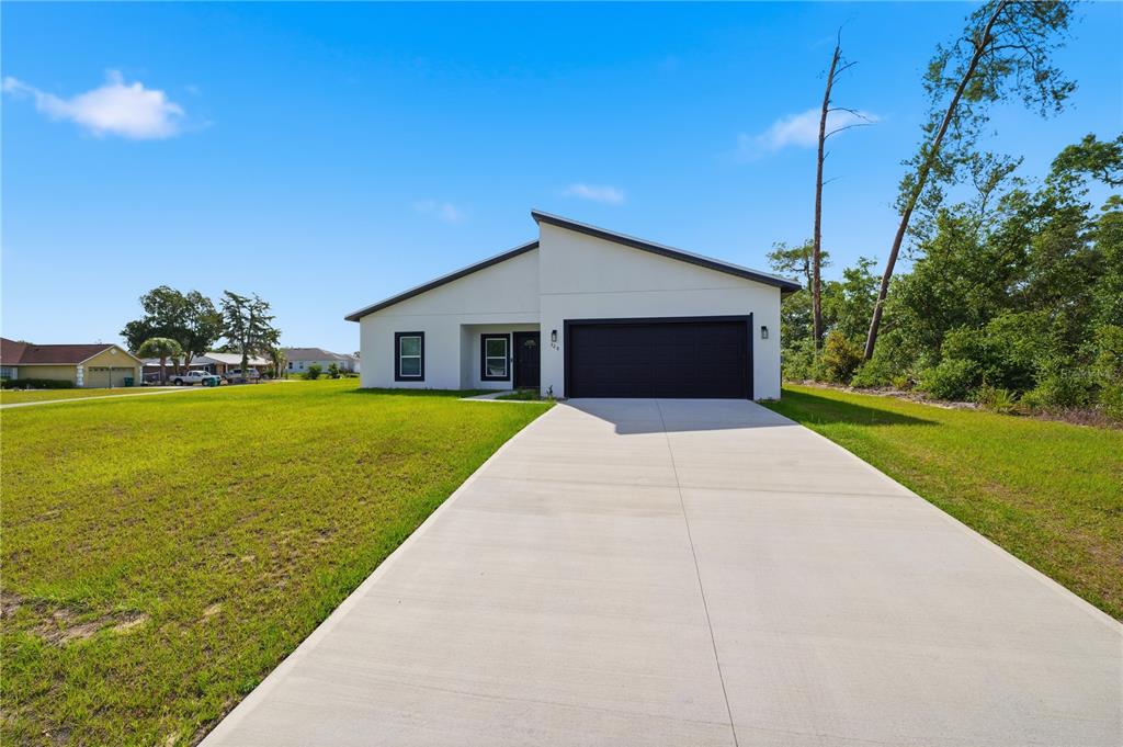 A single-story house with a white exterior, black garage door, and a concrete driveway — 320 MARION OAKS GOLF ROAD, OCALA, FL