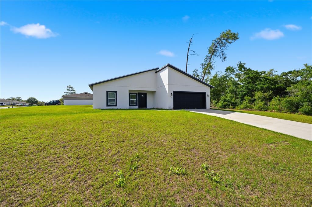 A modern, single-story white house with a black garage door and a concrete driveway — 320 MARION OAKS GOLF ROAD, OCALA, FL