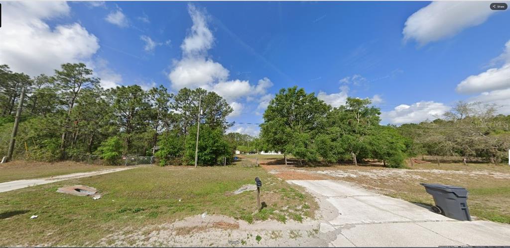 A gravel and concrete driveway leads to a wooded lot with a mailbox and trash bin — COMMONWEALTH AVE N, POLK CITY, FL