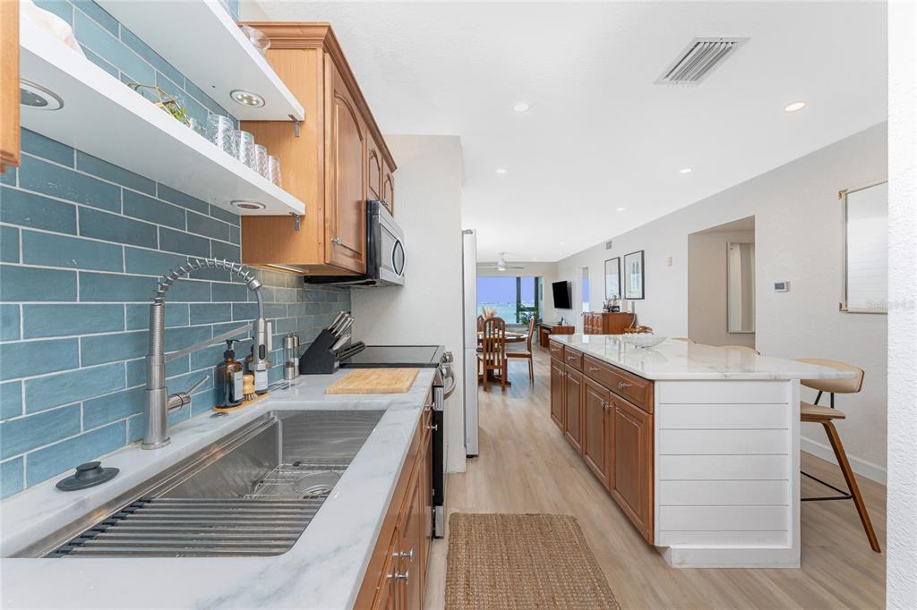 A kitchen features wood cabinets, a marble countertop, and a blue subway tile backsplash — 1500 PARK BEACH CIRCLE UNIT 3D, PUNTA GORDA, FL