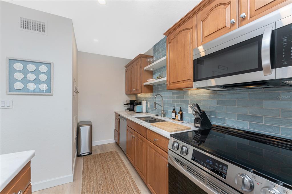 A kitchen features wood cabinets, a blue subway tile backsplash, and stainless steel appliances — 1500 PARK BEACH CIRCLE UNIT 3D, PUNTA GORDA, FL