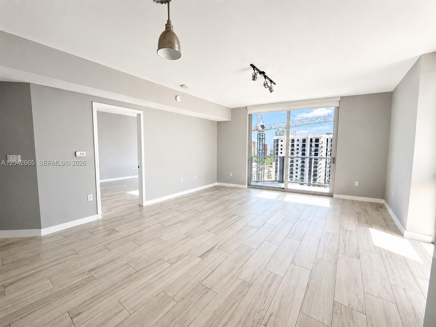An empty living room features light wood-look tile flooring, gray walls, and a sliding glass door — 1010 SW 2nd Ave # 1809, Miami FL 33130, MIAMI, FL
