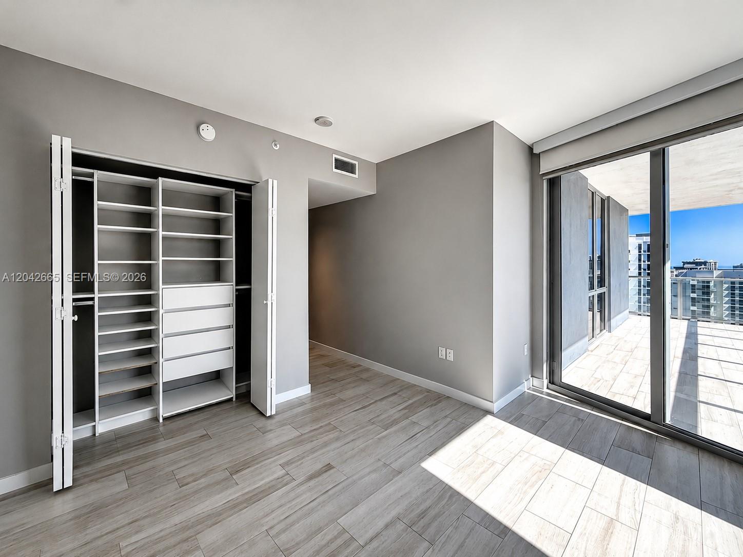 A room with gray walls, wood-look tile flooring, a built-in closet, and a balcony — 1010 SW 2nd Ave # 1809, Miami FL 33130, MIAMI, FL