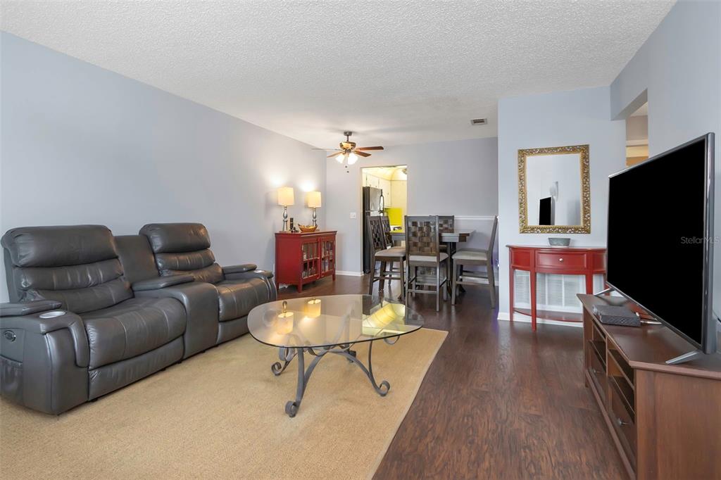 A living room with a gray sofa, glass coffee table, and dining area in back — 5246 81ST STREET N UNIT 24, ST PETERSBURG, FL