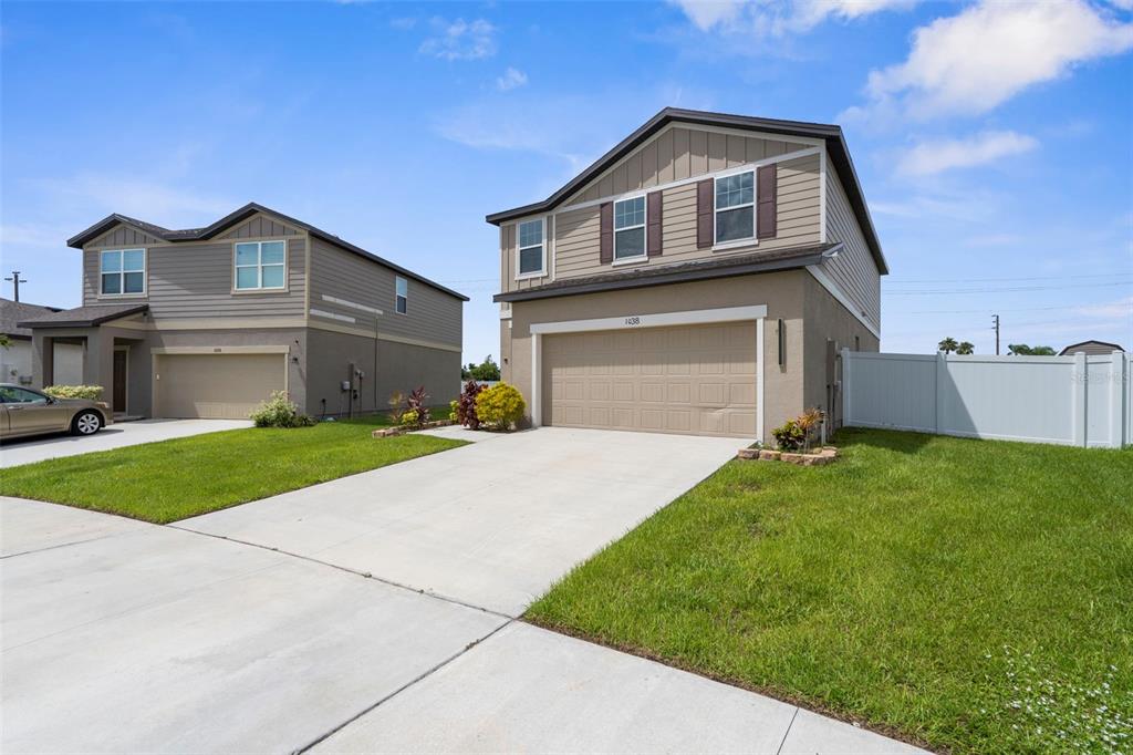 Two two-story suburban houses with beige stucco and siding exteriors stand side-by-side with concrete driveways — 1038 KELLY FERN LOOP, RUSKIN, FL