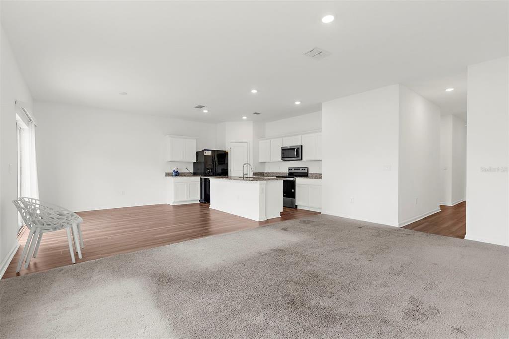 An open-concept kitchen and living area featuring white cabinets, dark countertops, and mixed flooring — 1038 KELLY FERN LOOP, RUSKIN, FL