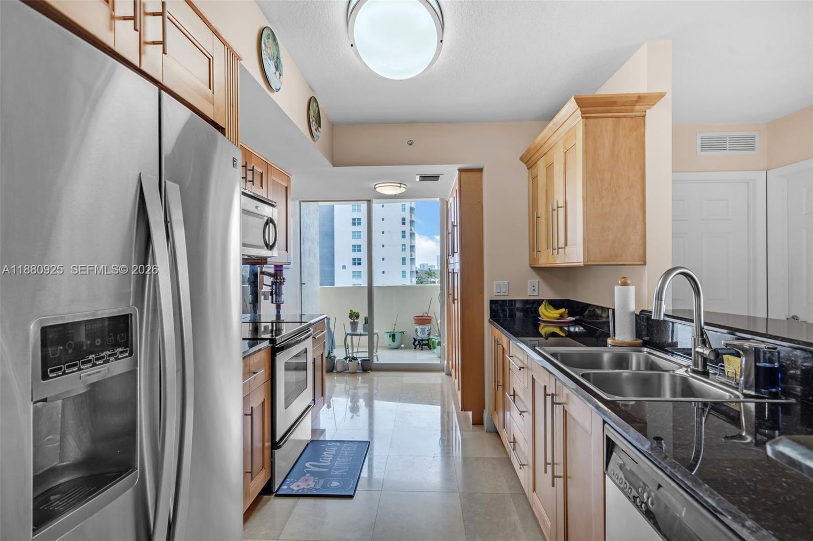 A kitchen features light wood cabinets, black countertops, stainless steel appliances, and a balcony view — 3232 SW 22nd Ter # 801, Miami FL 33145, MIAMI, FL