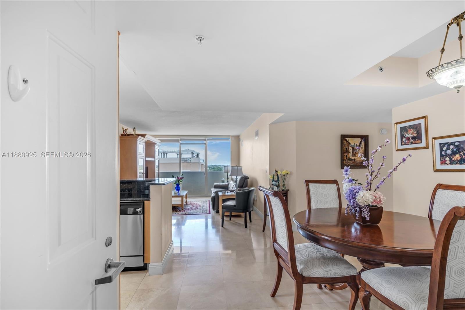 This interior view shows a dining area and kitchen leading to a living room with balcony — 3232 SW 22nd Ter # 801, Miami FL 33145, MIAMI, FL