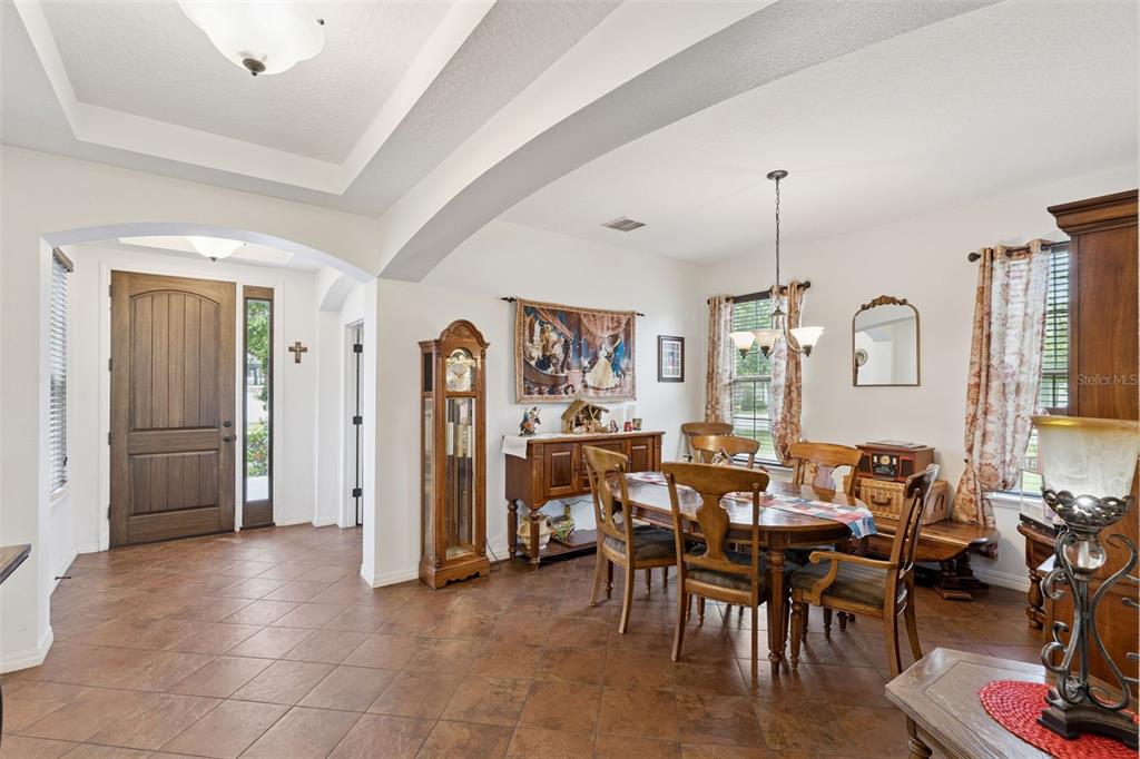 A dining room with tile floors, a wooden table, and a grandfather clock near an entryway — 9189 BUSACO PARK WAY, WINTER GARDEN, FL