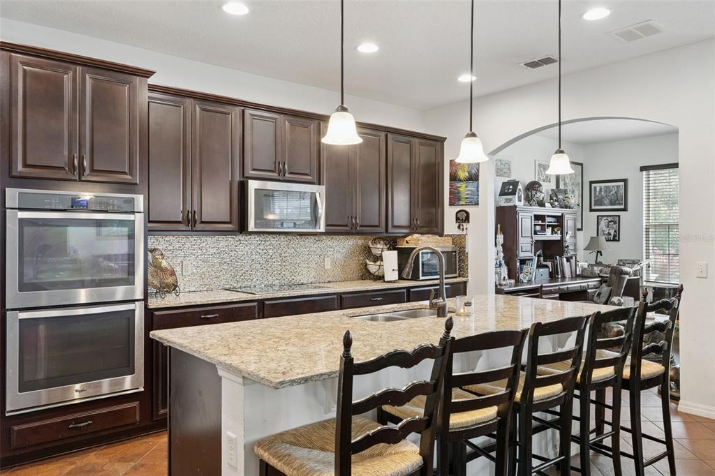 A kitchen with dark wood cabinets, granite countertops, a center island, and stainless steel appliances — 9189 BUSACO PARK WAY, WINTER GARDEN, FL
