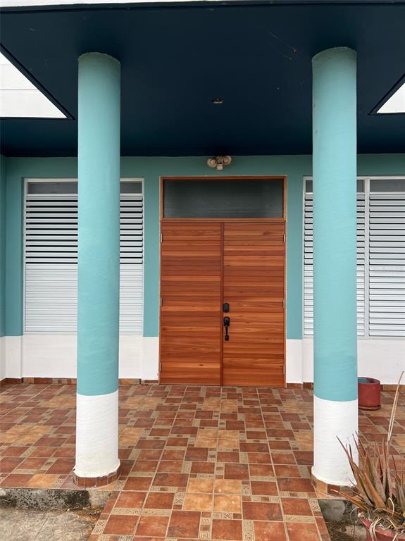 A covered porch features two teal columns, a wooden double door, and tiled flooring — Circulo C CASA EN RAMEY UNIT 213-A, AGUADILLA, PR