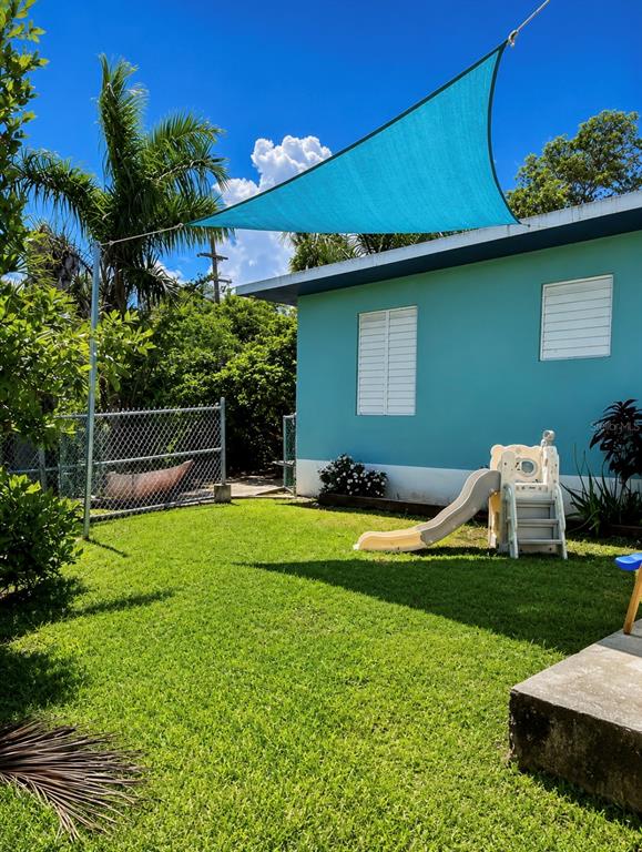 A turquoise house exterior features a blue shade sail, a small slide, and a lawn — Circulo C CASA EN RAMEY UNIT 213-A, AGUADILLA, PR