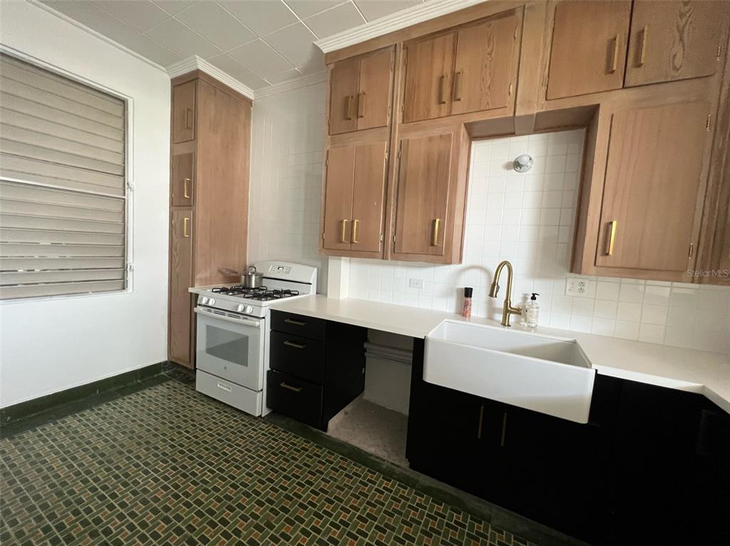 A kitchen features wood upper cabinets, black lower cabinets, a farmhouse sink, and patterned tile flooring — Circulo C CASA EN RAMEY UNIT 213-A, AGUADILLA, PR