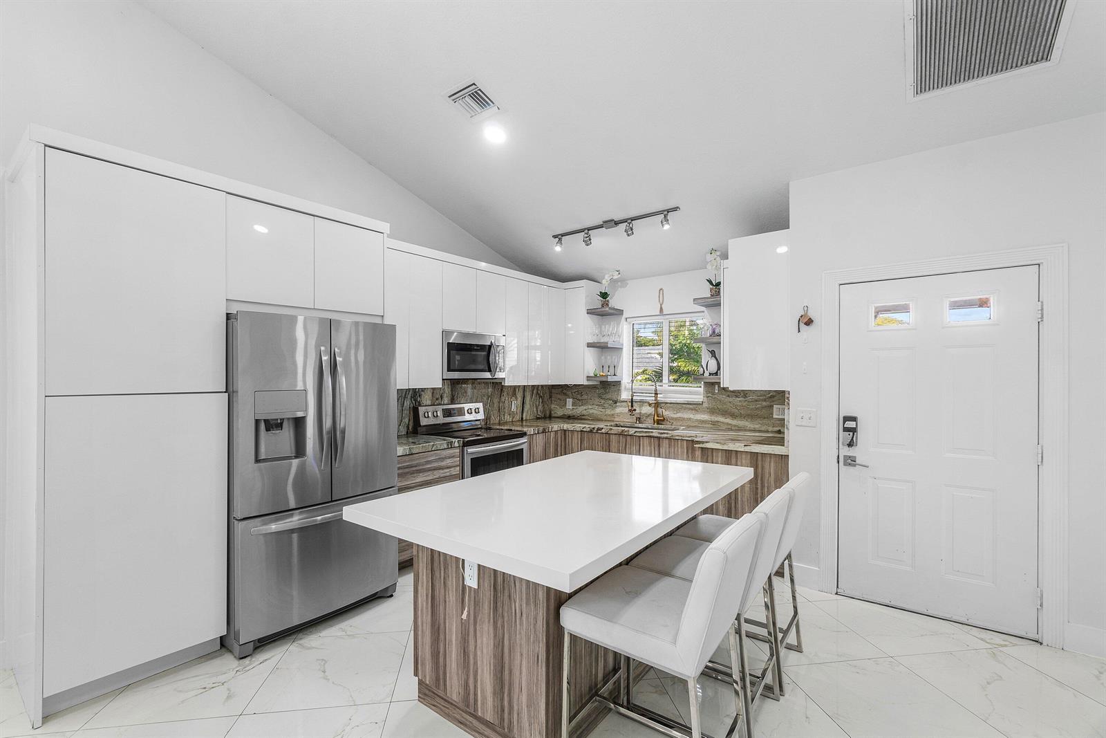 A modern kitchen features white cabinetry, stainless steel appliances, a center island, and marble flooring — 101 Azalea Circle, Boynton Beach FL 33436, BOYNTON BEACH, FL