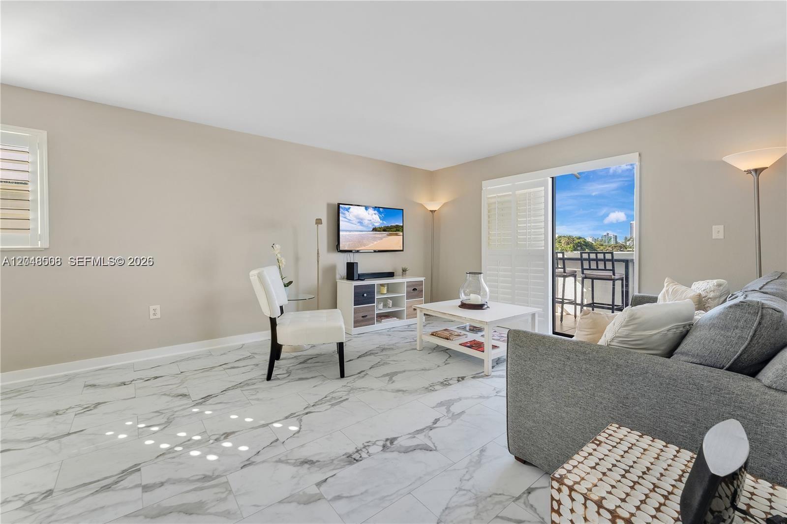 A living room features marble-look tile flooring, a grey sofa, and a balcony with seating — 1418 Collins Ave # 504, Miami Beach FL 33139, MIAMI BEACH, FL