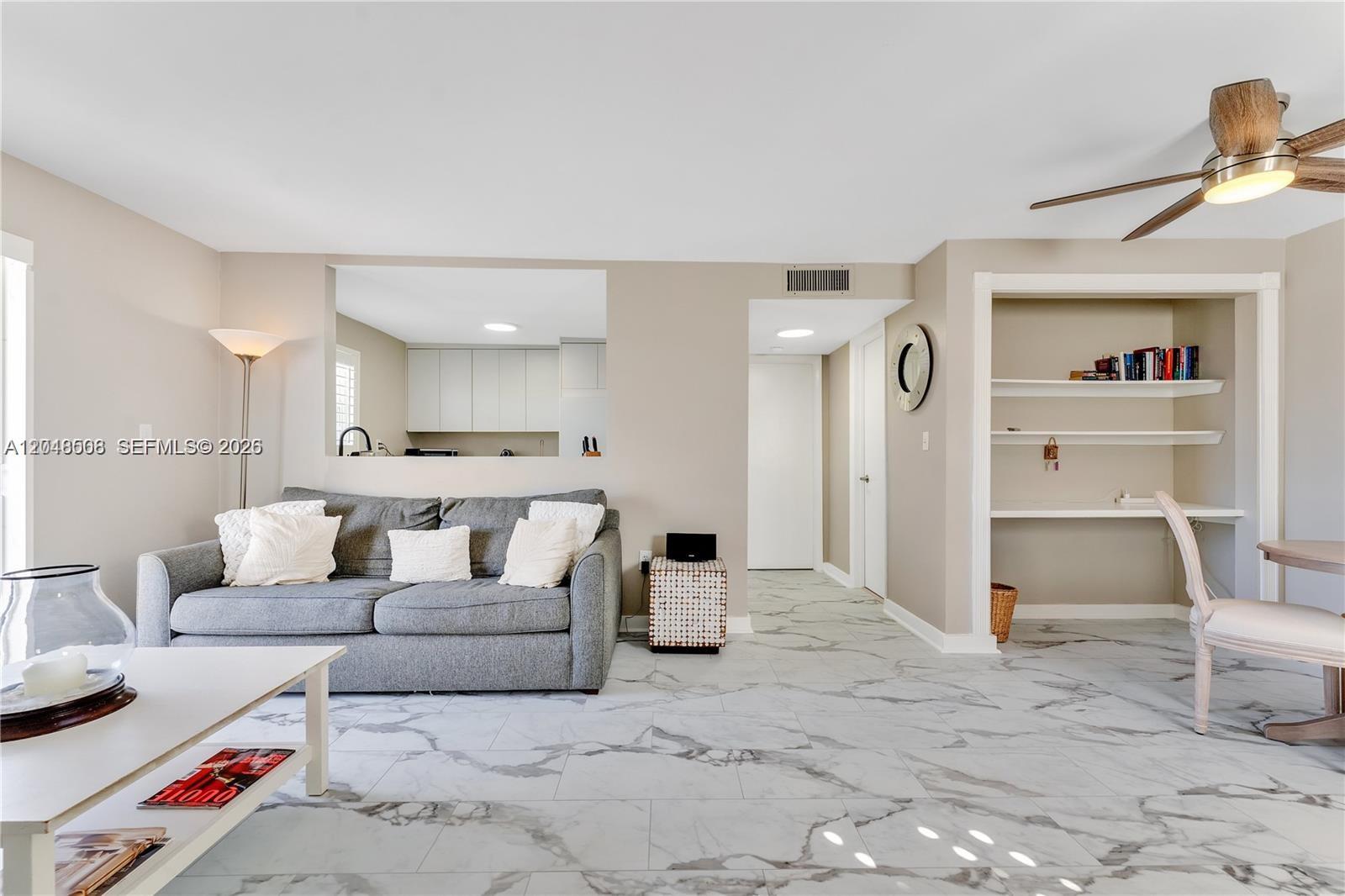 A living room features gray tile flooring, a gray sofa, and a built-in desk area — 1418 Collins Ave # 504, Miami Beach FL 33139, MIAMI BEACH, FL