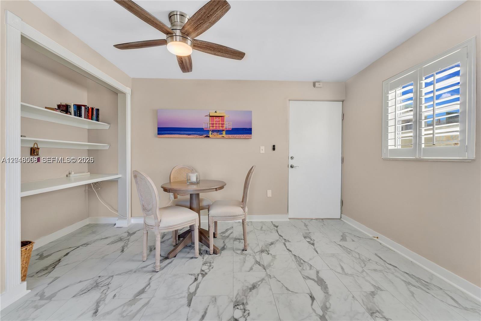 A dining area features a small round table, two chairs, built-in shelving, and marble flooring — 1418 Collins Ave # 504, Miami Beach FL 33139, MIAMI BEACH, FL