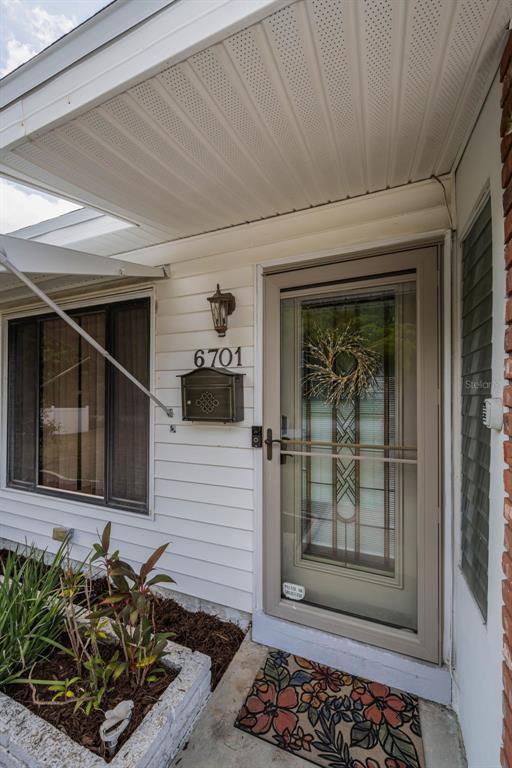 A front entryway features a white-sided exterior, a storm door, a mailbox, and a planter — 6701 ORCHARD DRIVE N, ST PETERSBURG, FL