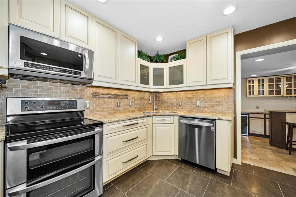 A kitchen features cream-colored cabinets, stainless steel appliances, a tiled backsplash, and dark floor tiles — 6701 ORCHARD DRIVE N, ST PETERSBURG, FL
