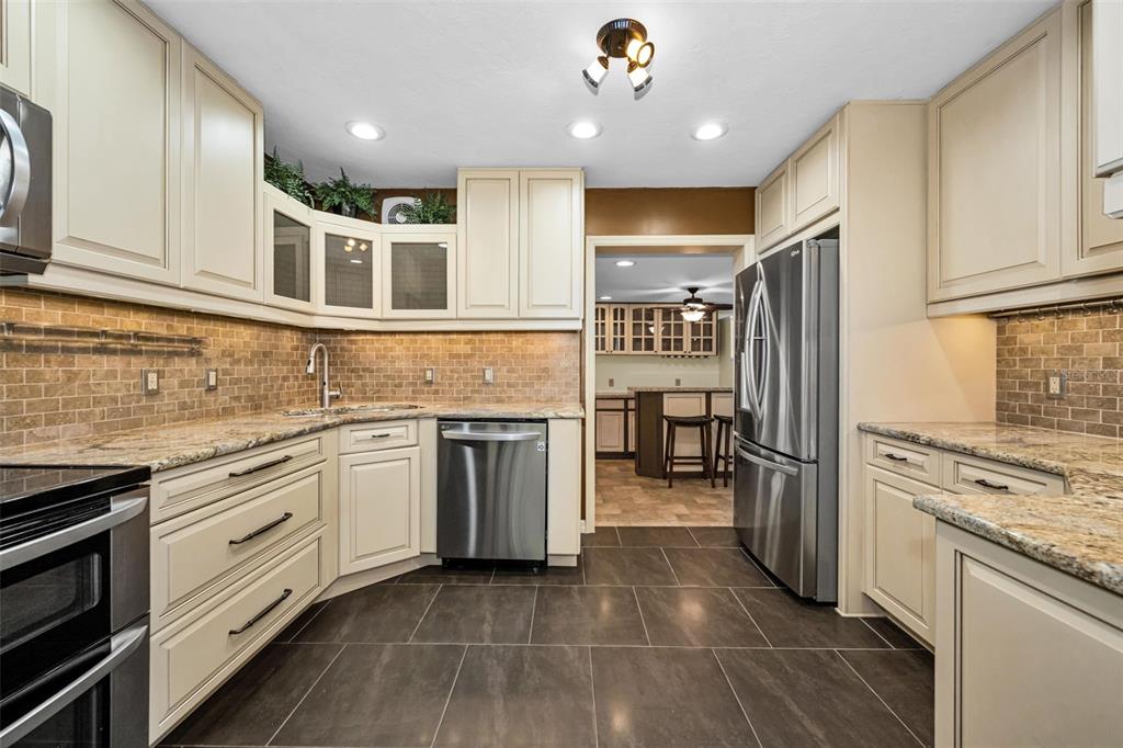 A kitchen features cream cabinets, granite countertops, a brick backsplash, and dark tile flooring — 6701 ORCHARD DRIVE N, ST PETERSBURG, FL