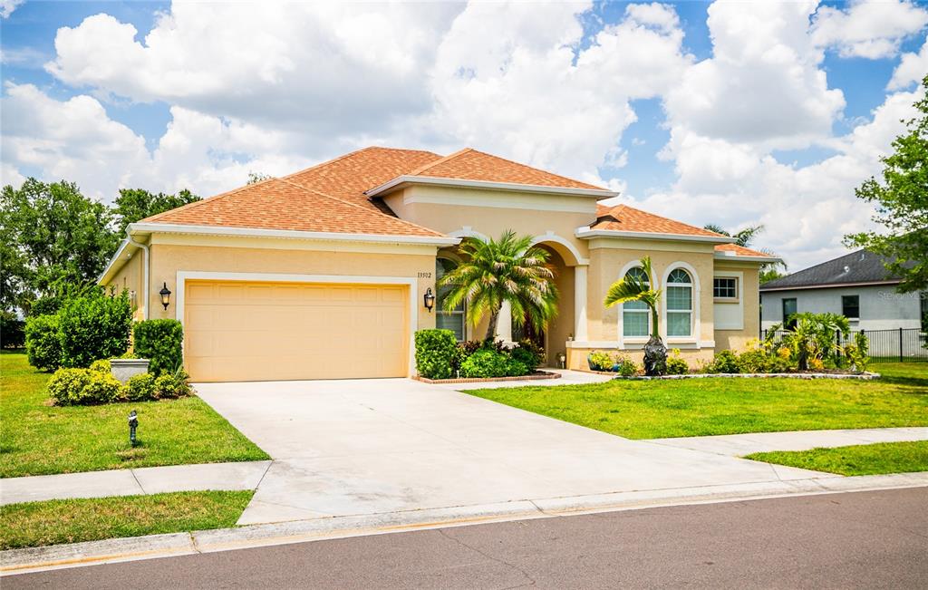 A single-story tan stucco house with a two-car garage and a palm tree in front — 13502 22ND COURT E, PARRISH, FL